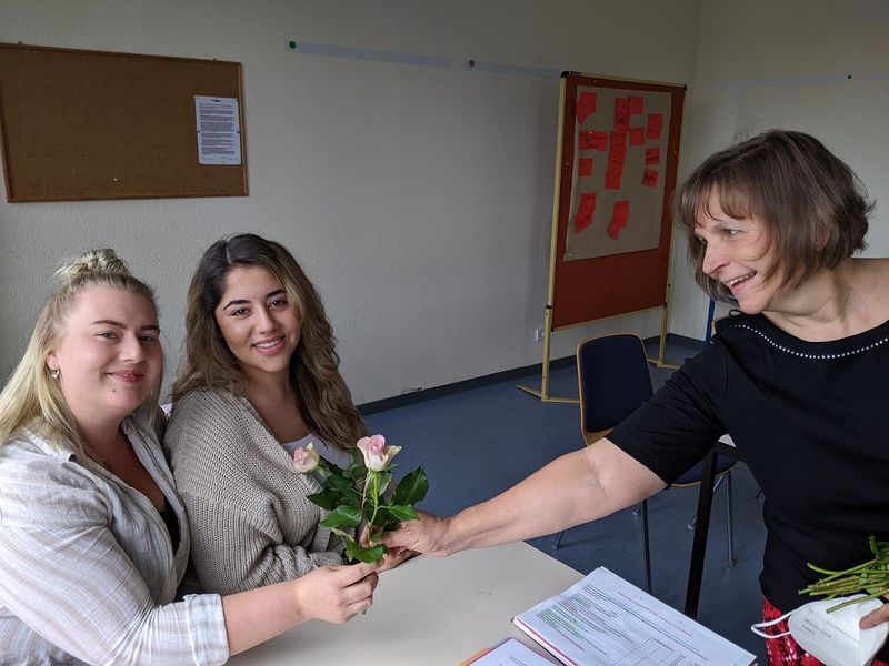 Klassenleitung überreicht an zwei Schülerinnen eine Blume
