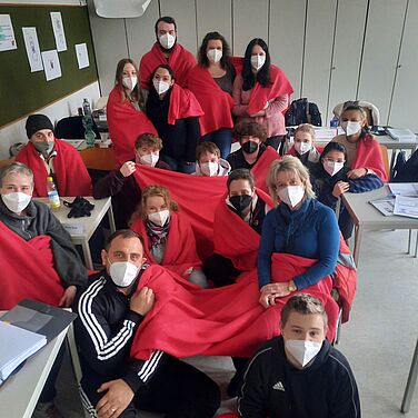 Schüler sitzen auf dem Boden des Klassenzimmers mit roten Decken