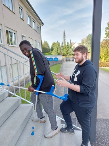 Mann mit Krücken steigt Treppe hinauf und wird von einem anderen Mann geholfen