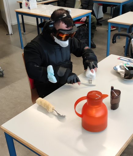 Junger Mann sitzt in Winterkleidung und Skibrille am Tisch und simuliert so eine Sehschwäche